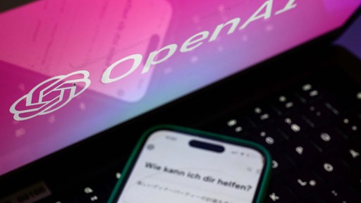 Ein Smartphone mit dem KI-Chatbot ChatGPT ist vor dem Logo des US-Softwareunternehmens OpenAI zu sehen. 