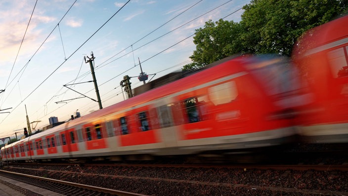 Eine S-Bahn fährt am frühen Morgen Richtung Kölner Innenstadt. Im Hintergrund ist der Fernmeldeturm Colonius zu sehen.