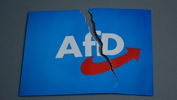 Eine Karte, auf der das Logo der AfD zu sehen ist, hat einen Riss. Symbolbild
