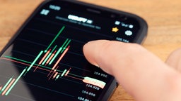 Symbolbild: Ein Finger berührt ein Diagramm auf dem Bildschirm eines Smartphones, das auf einem Schreibtisch liegt.