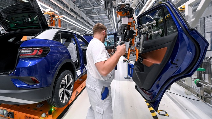 Ein Mitarbeiter in einem Autowerk hängt eine Tür in einen blauen Wagen ein.