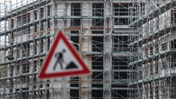 Symbolbild: Baustellenschild vor der Baustelle eines mehrstöckigen Gebäudes.