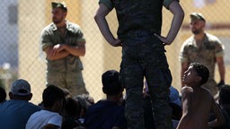 Ein junger Migrant blickt in der spanischen Exklave Ceuta am 2. August 2026 auf einen Angehörigen der Infanterieeinheit „Regulares“ der spanischen Armee, nahe dem Grenzposten, bevor die Gruppe nach Marokko zurückgebracht wird.