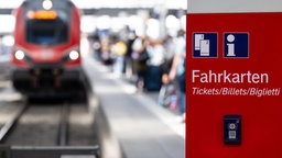 Ein Fahrkartenautomat der Deutschen Bahn, dahinter sieht man ein Gleis, an dem ein Regionalzug hält.