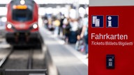 Ein Fahrkartenautomat der Deutschen Bahn, dahinter sieht man ein Gleis, an dem ein Regionalzug hält.
