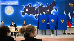 Mitglieder der lokalen Wahlkommission sitzen neben Wahlkabinen in einem Wahllokal in Novosibirsk in Russland.