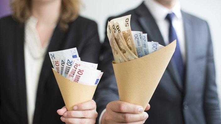 Eine Frau und ein Mann halten unterschiedlich große Tütchen mit Geld hoch