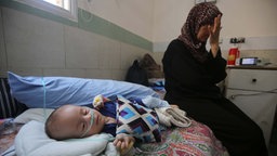symbolbild: Ein unterernährtes Kind und eine besorgte Erwachsene im Krankenhaus (Gaza 2025).