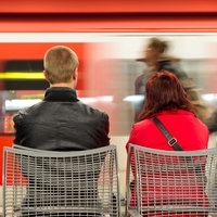 Symbolbild: Menschen sitzen an einem Bahnsteig, an dem eine S-Bahn vorbeifährt.