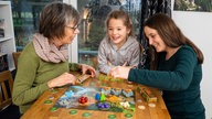 Symbolbild: Drei Menschen unterschiedlichen Alters spielen ein Gesellschaftsspiel.