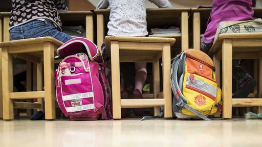 Symbolbild: Kinder sitzen mit ihren Schulranzen in einem Klassenzimmer am Tisch