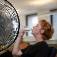Eine Frau sitzt vor einem Tischventilator und trinkt aus einer Flasche Wasser