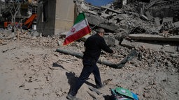 Ein Mann trägt eine iranische Flagge und legt sie auf die Trümmer einer Polizeieinrichtung, die während der amerikanisch-israelischen Militäraktion getroffen wurde.