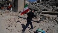 Ein Mann trägt eine iranische Flagge und legt sie auf die Trümmer einer Polizeieinrichtung, die während der amerikanisch-israelischen Militäraktion getroffen wurde.