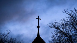 Dunkle Wolken ziehen über das Kreuz auf einer Kirche hinweg.