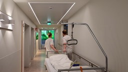 Symbolbild: Zwei Pflegekräften ziehen ein Krankenbett durch einen Klinikflur.