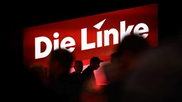 Symbolbild: Vor dem Logo der Partei "Die Linke" laufen Menschen vorbei.