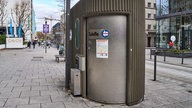 Eine öffentliche Toilette in der Innenstadt von Stuttgart, ausgestattet mit einem Zugangssystem und Informationen zu weiteren Standorten. 