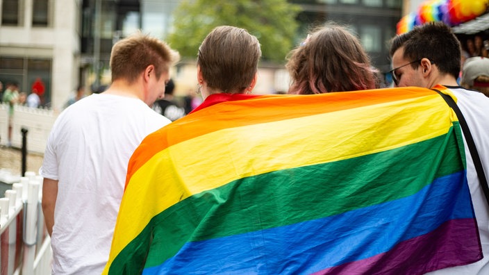 Vier junge Menschen mit Regenbogenfahne auf dem CSD am 5.8.2023 in Nuernberg.