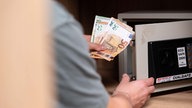 Symbolbild: Ein Mensch legt Bargeld in einen kleinen Safe (Hotel).