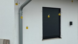 Mit gelben Polizeimarkierungen versehene Einschusslöcher an einer Wohnhaus-Wand mit einem Fenster, das mit einem Rollladen verschlossen ist