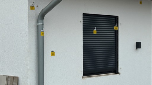 Mit gelben Polizeimarkierungen versehene Einschusslöcher an einer Wohnhaus-Wand mit einem Fenster, das mit einem Rollladen verschlossen ist