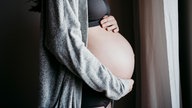 Schwangere Frau legt ihre Hände auf den Bauch
