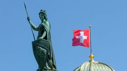 Die Helvetia-Statue vor einer Schweizer Flagge am Schweizer Parlamentsgebäude (Bundeshaus). 