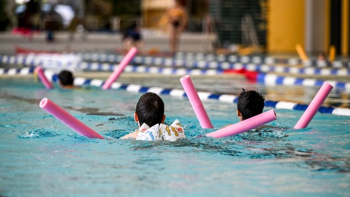 Kinder mit Badenudeln im Schwimmbad