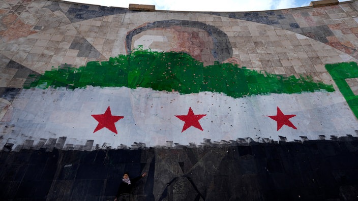  Ein syrischer Junge steht unter einem riesigen Porträt des verstorbenen syrischen Präsidenten Al-Assad, übermalt mit den Farben der sogenannten "revolutionären" Flagge.