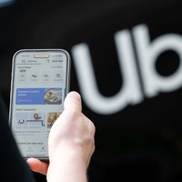 Symbolbild: Uber-App auf einem Smartphone-Display neben dem Schriftzug "Uber".