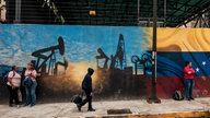 Menschen gehen an einem Wandgemälde von Öltürmen am Hauptsitz von "Petróleos de Venezuela" in Caracas vorbei.
