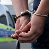Symbolbild: Eine Person mit Handschellen vor einem Polizeiauto
