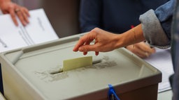 Eine Frau wirft einen Stimmzettel in eine Wahlurne.