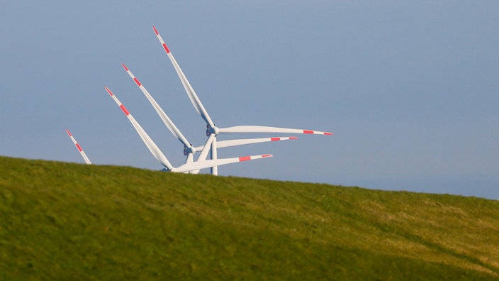 Schleswig-Holstein, Dagebüll: Die Sonne scheint auf Windräder, die hinter einem Deich stehen. 