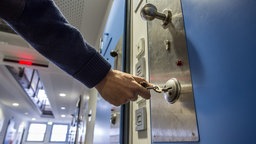 Symbolbild: Eine Person schließt eine Gefängniszelle auf oder ab.