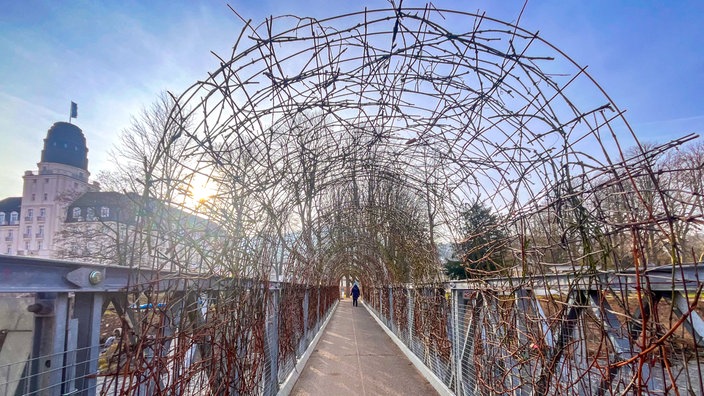 Fußgängerbrücke in Bad Neuenahr-Ahrweiler mit markanter, bogenförmiger Gestaltung aus verflochtenen Zweigen.
