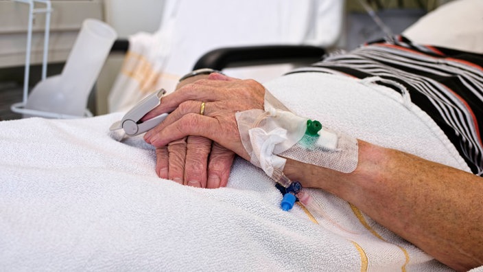 Hände eines alten Mannes mit Kanüle im Krankenbett 