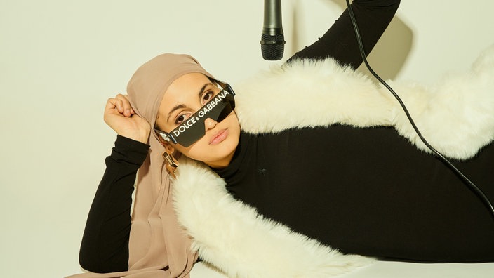 Comedienne Anissa Loucif liegt lässig auf dem Boden, während über ihr ein Mikrofon hängt.