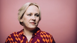 Die Porträtaufnahme zeigt Anne Rabe vor rosa Hintergrund, den Blick in die Ferne gerichtet.