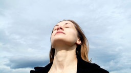 Eine Frau hat den Kopf gen Himmel gerichtet, die Augen geschlossen und atmet ein