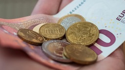 Eine Hand hält einen Geldschein und Münzen