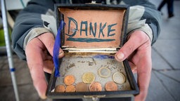 Blick in eine offene Holzkiste mit Münzen und einem Schild "Danke"
