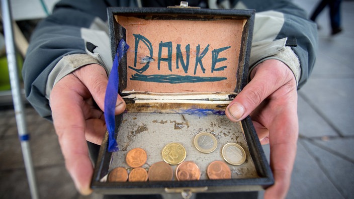 Blick in eine offene Holzkiste mit Münzen und einem Schild "Danke"
