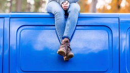 Eine Frau sitzt entspannt mit verschränkten Füßen auf dem Dach eines blauen Busses 