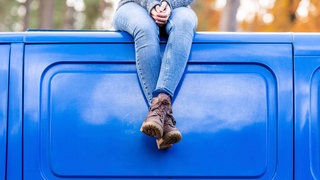 Eine Frau sitzt entspannt mit verschränkten Füßen auf dem Dach eines blauen Busses 