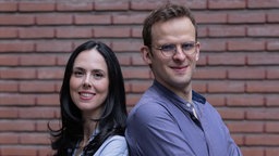 Die Psychoanalytiker:innen Cécile Loetz und Jakob Müller stehen Rücken an Rücken und blicken in die Kamera.