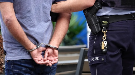 Ein Mann in Handschellenwird von einem Polizisten abgeführt.