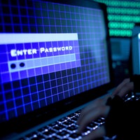 Ein Passwort wird auf einem Laptop über die Tastatur eingegeben, im Hintergrund weitere Bildschirme.