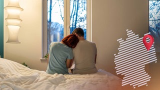 Paar sitzt auf einem Bett und schaut aus dem Fenster